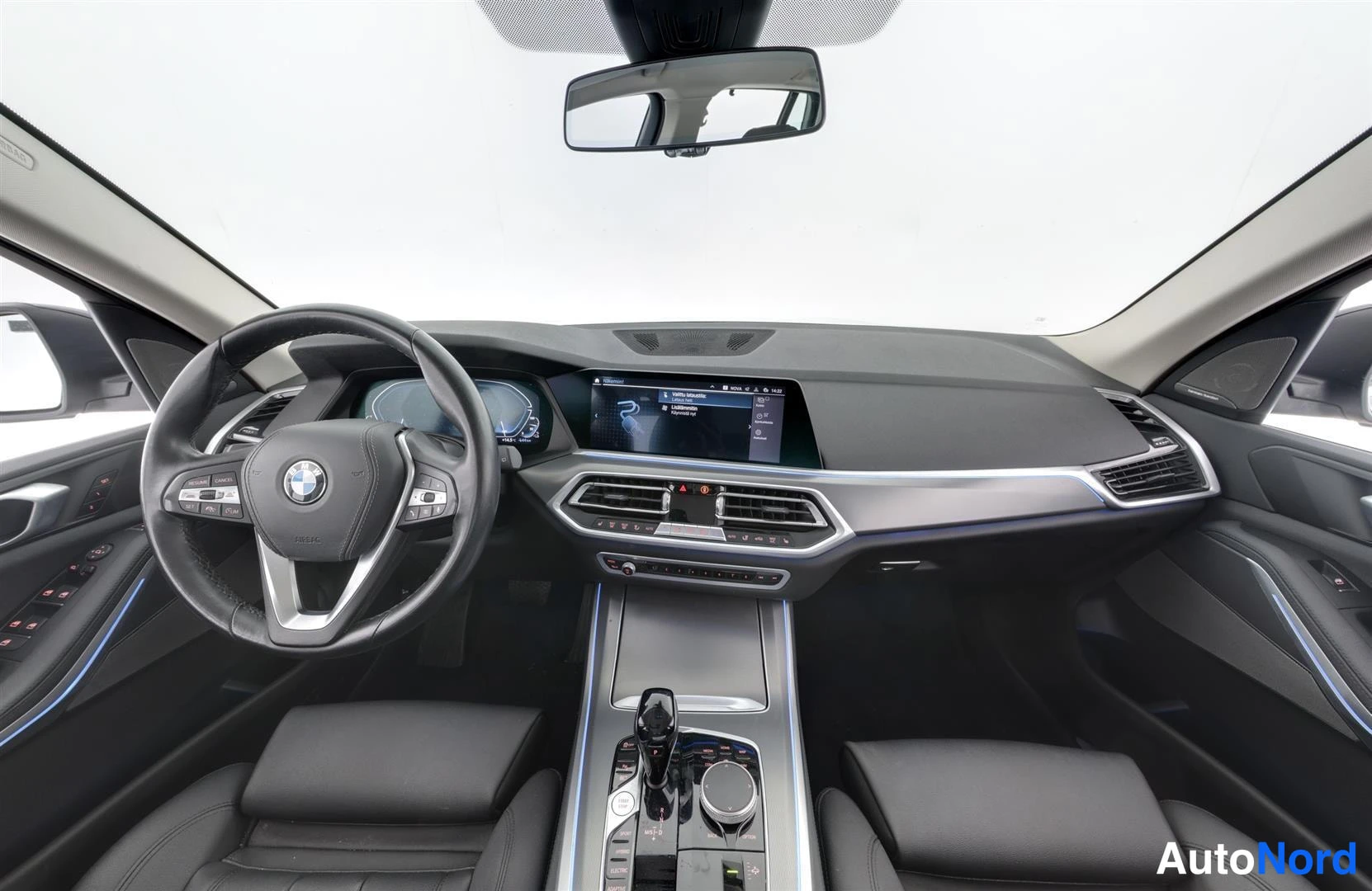 Etuistuimet: Ohjaamon näkymä: BMW-ohjauspyörä, kosketusnäyttö, vaihteenvalitsin ja tummat istuimet.