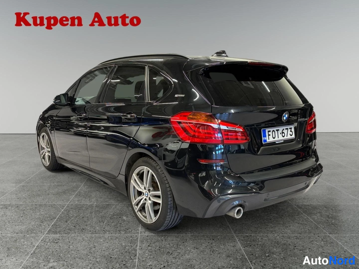 Takaviisto: Musta BMW 2-sarjan Active Tourer takaa oikealta kolmanneskulmassa showroomissa.