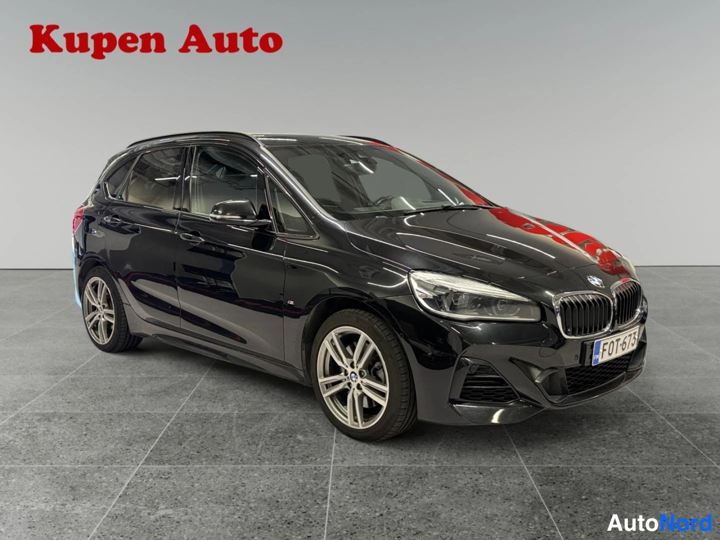 Etuviisto, nokka oikealle: Musta BMW 2-sarjan Active Tourer edestä oikealta kolmanneskulmassa showroomissa.