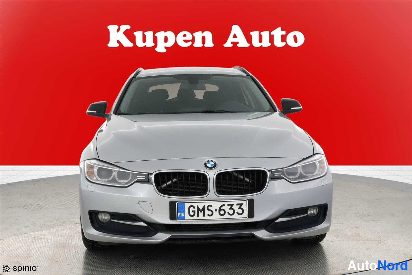 Edestä: Hopeanharmaan BMW:n suora etunäkymä, rekisteriksi, punainen tausta.