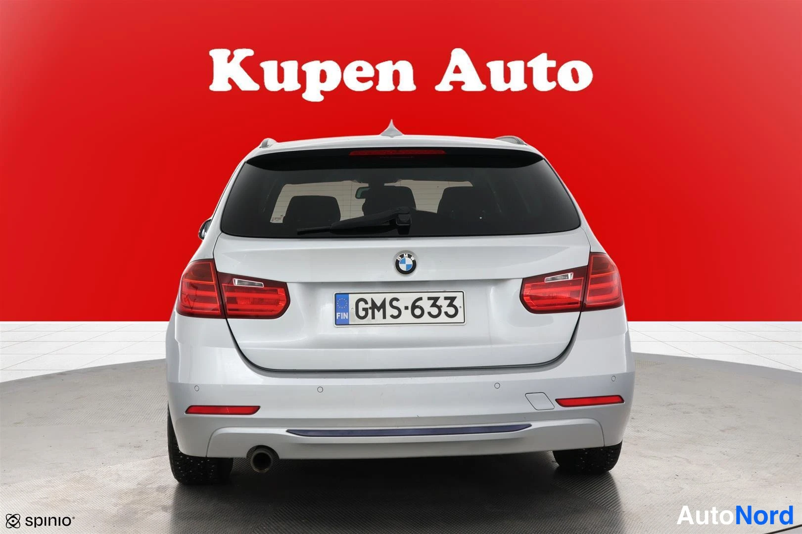 Takaa: BMW Farmarin takaosa suoraan takaa, rekisterikilpi, hopea koripaneeli punaista taustaa vasten.