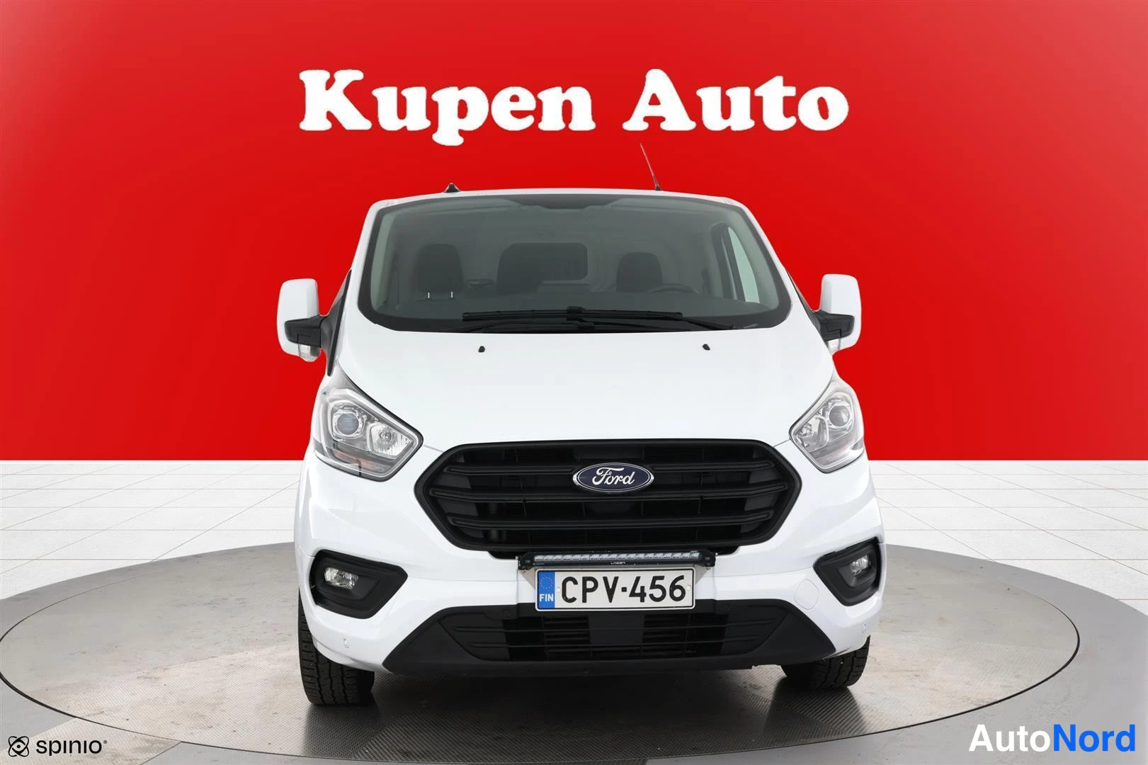 Edestä: Valkoisen Ford Transit Custom -pakettiauton etupää suoraan edestä punaisella taustalla