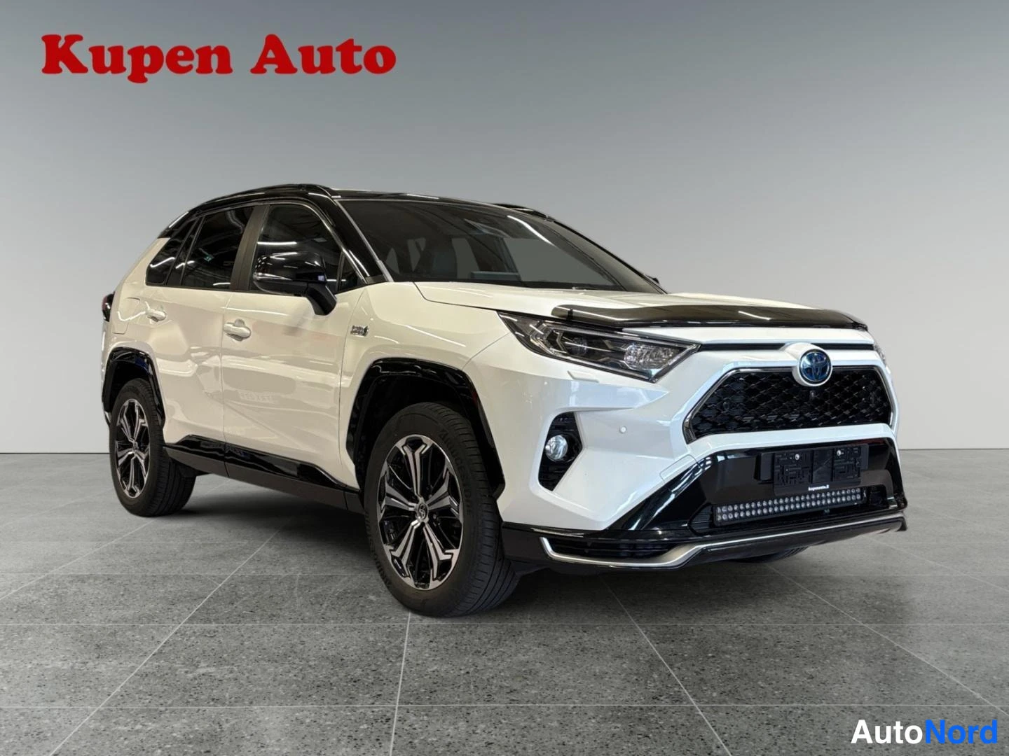 Etuviisto, nokka oikealle: Valkoinen Toyota RAV4, etukulmanäkymä oikealta, musta etuspoileri ja kattokaari, hopeavanteet.