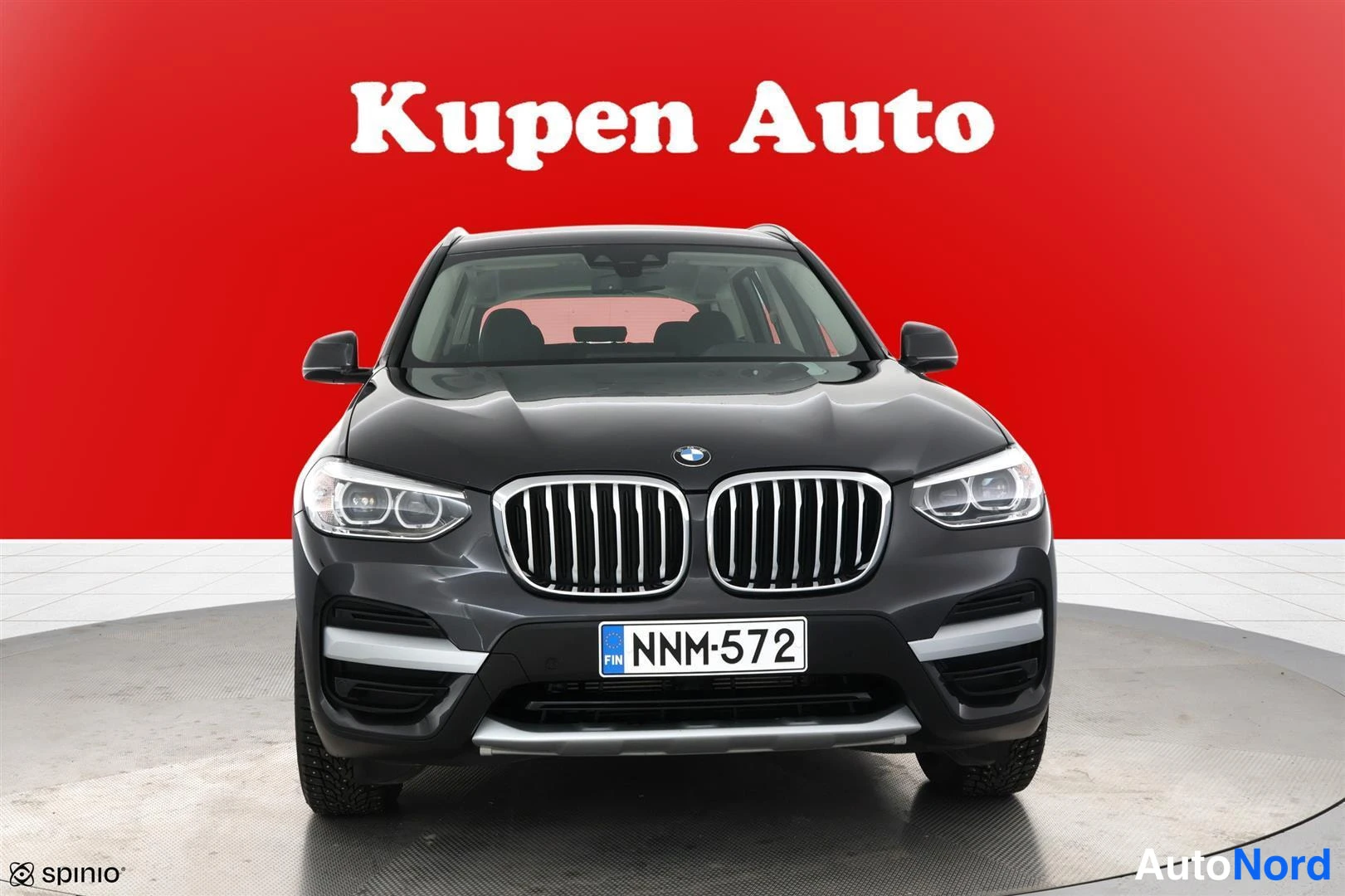 Edestä: BMW X3 suoraan edestä valokuvattuna punaista taustaa vasten.