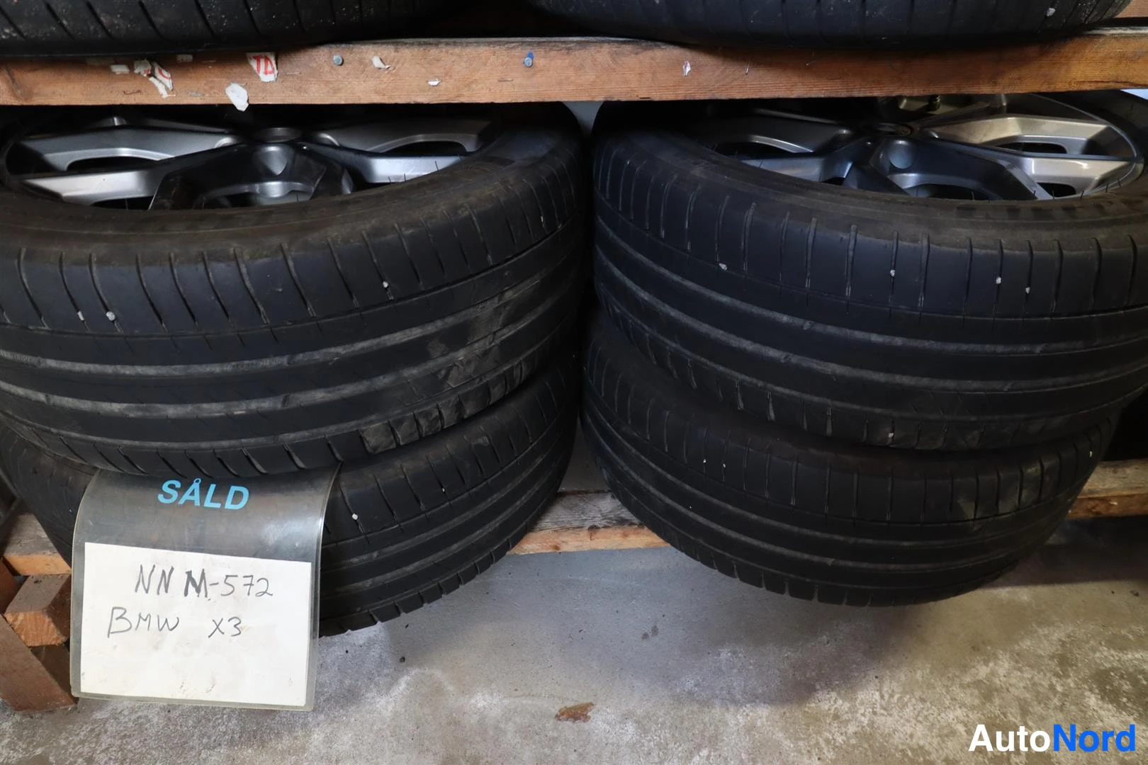 Muu: Kesärengassetti alumiinivanteilla hyllyllä; lapussa käsiala "NN M-572 BMW X3" ja merkintä SÄLD.