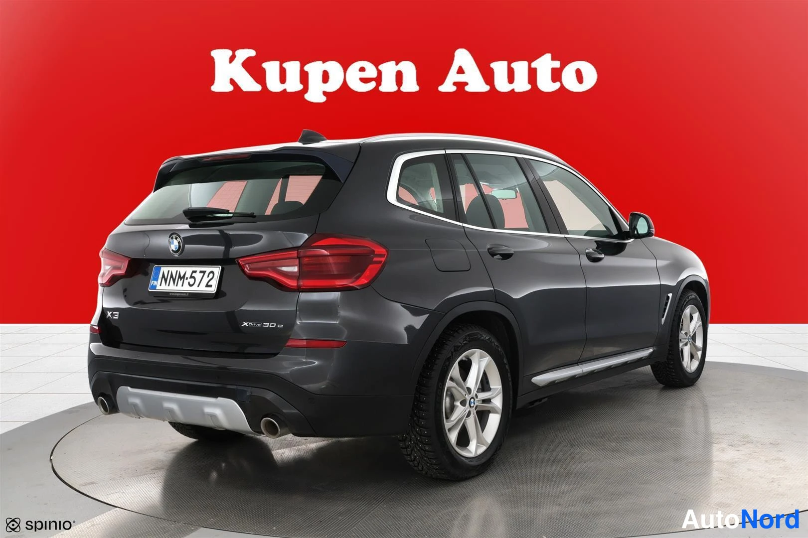 Takaviisto: Auton takakulmanäkymä: tummanharmaa BMW X3 -maasturi, takavalojen, takaluukun ja oikean kyljen onnistunut kuva punaisella taustalla.