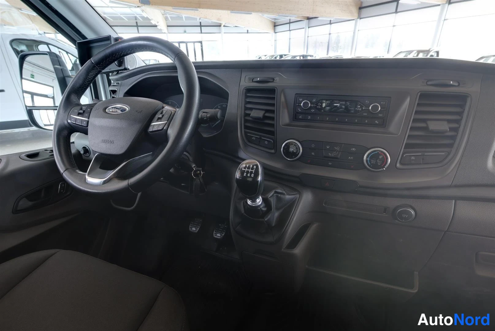 Ohjaamo: Ford Transitin kojelauta ja ratti lähikuvassa, manuaalivaihde ja radio/ilmastointisäätimet