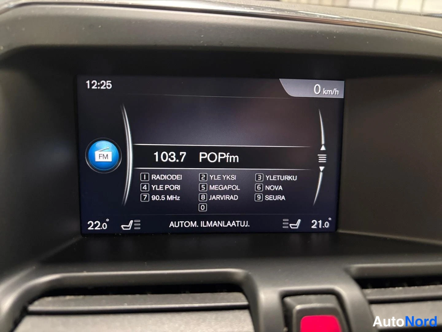 Yksityiskohta: Keskikonsoleen näyttö: radio 103.7 POPfm ja automaattinen ilmastointi -teksti.