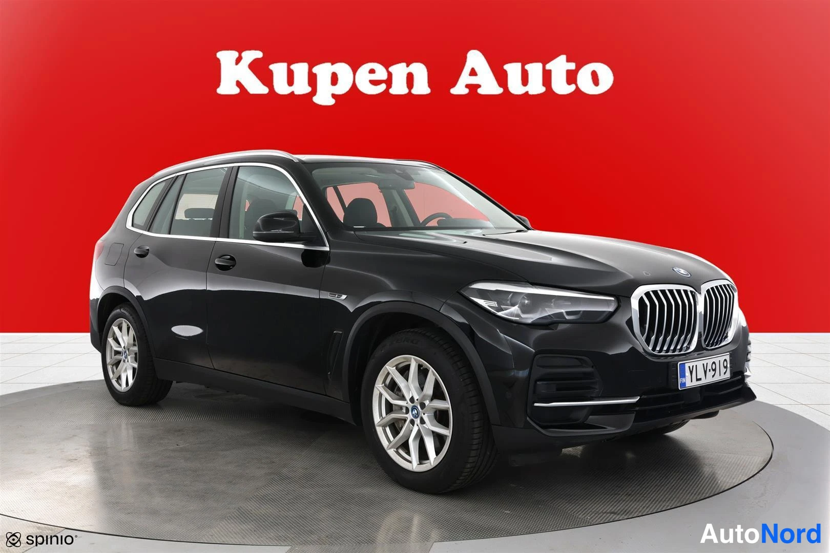 Etuviisto, nokka oikealle: Musta BMW X5 -maasturi kulmassa edestä vasemmalta, rekisteritunnus, punainen tausta.