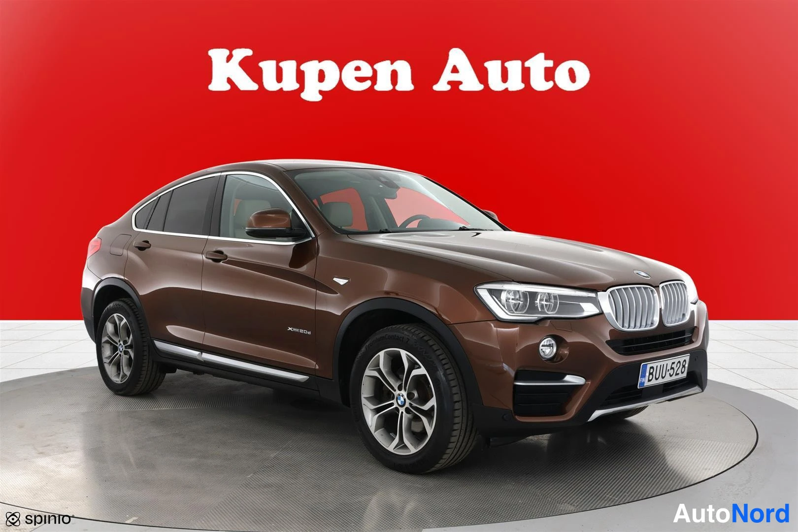 Etuviisto, nokka oikealle: Ruskea BMW X4 kulmakuva punaisella taustalla, Kupen Auto -logo ylhäällä, rekisteritunnus.