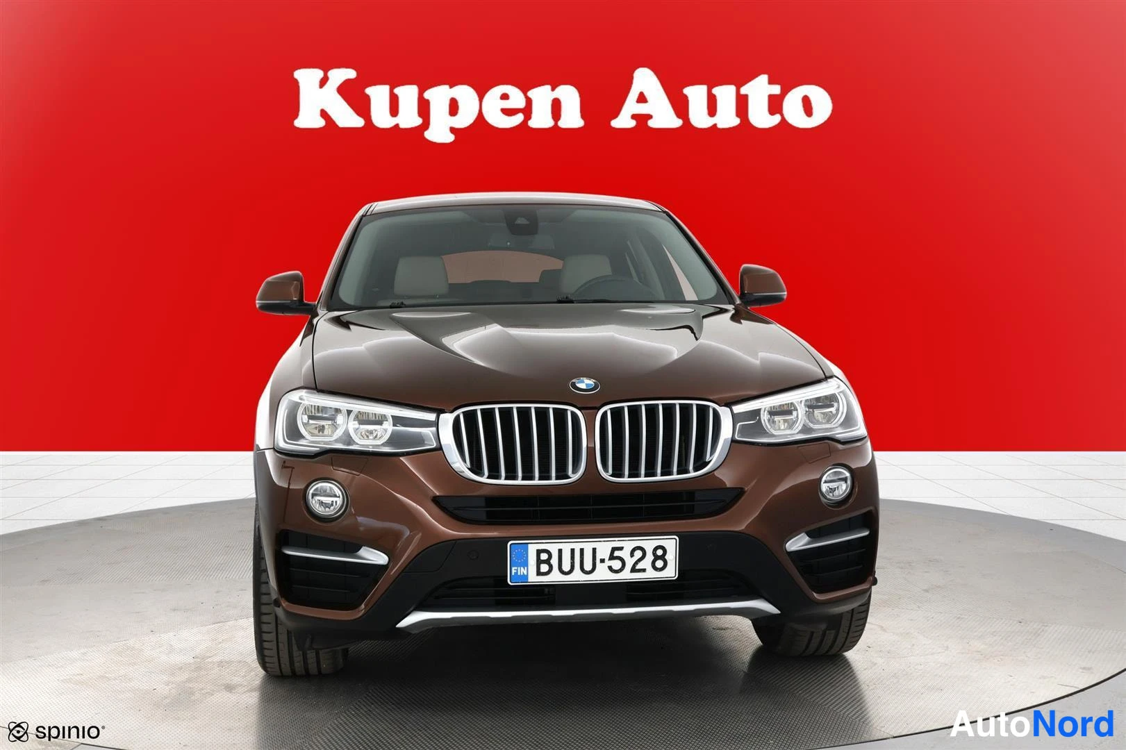 Edestä: Ruskean BMW X4:n etukuva suoraan edestä, punainen tausta ja rekisteritunnus.
