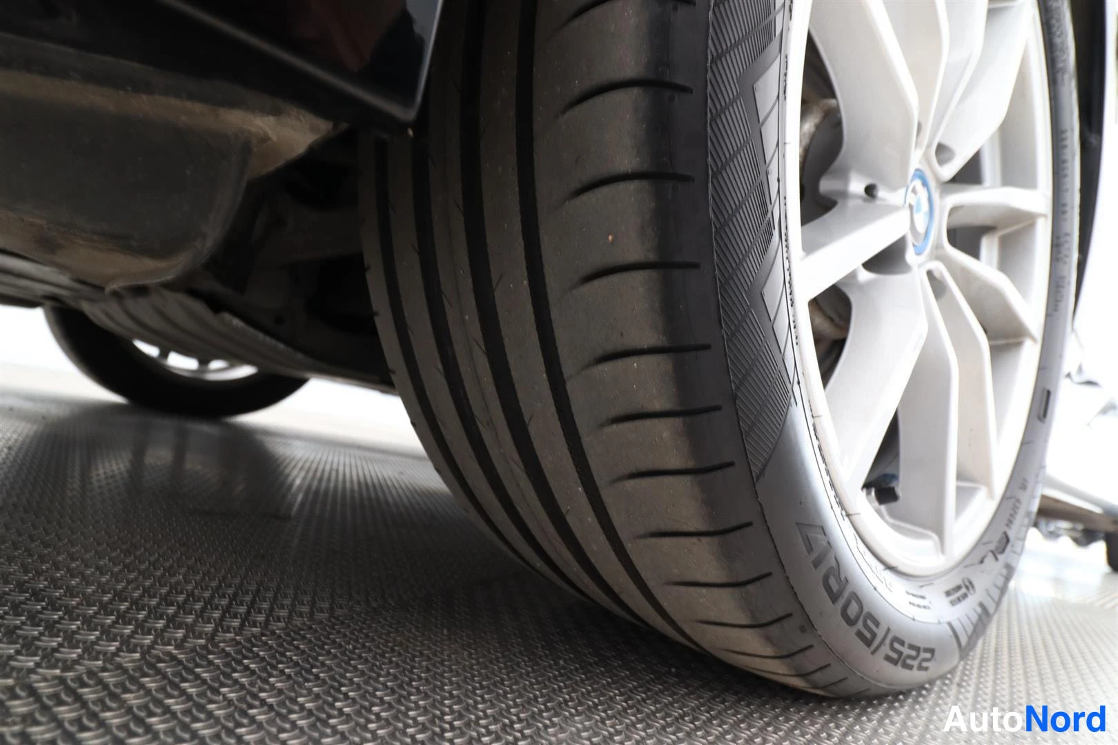 Yksityiskohta: Mustan auton takapyörän rengas lähikuva; seinässä lukee '225/50R4', hopeavanne, auto nostettuna.