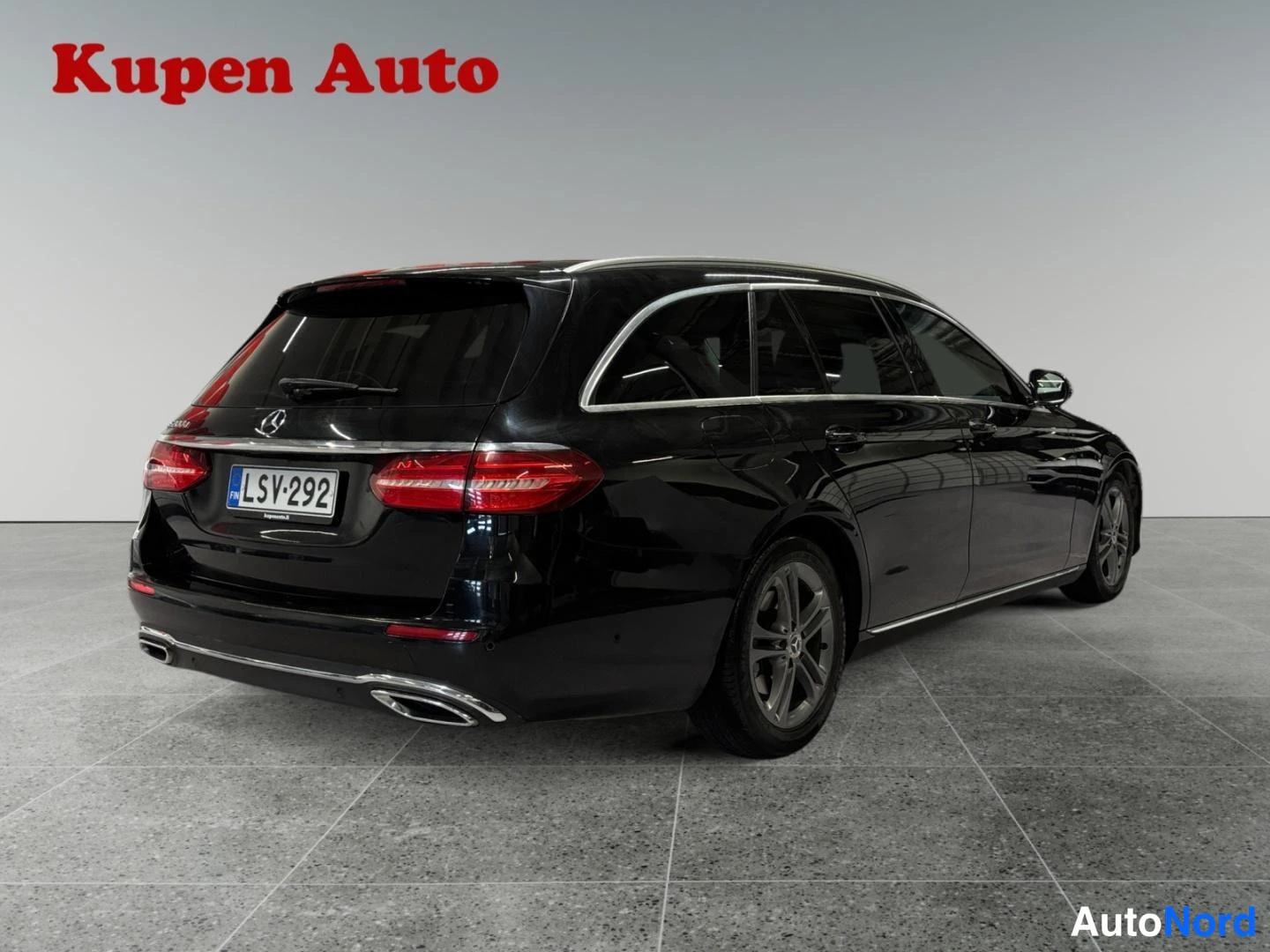 Takaviisto: Musta Mercedes-Benz E-sarjan farmari takaa vasemmalta kolmivartalokuvassa.