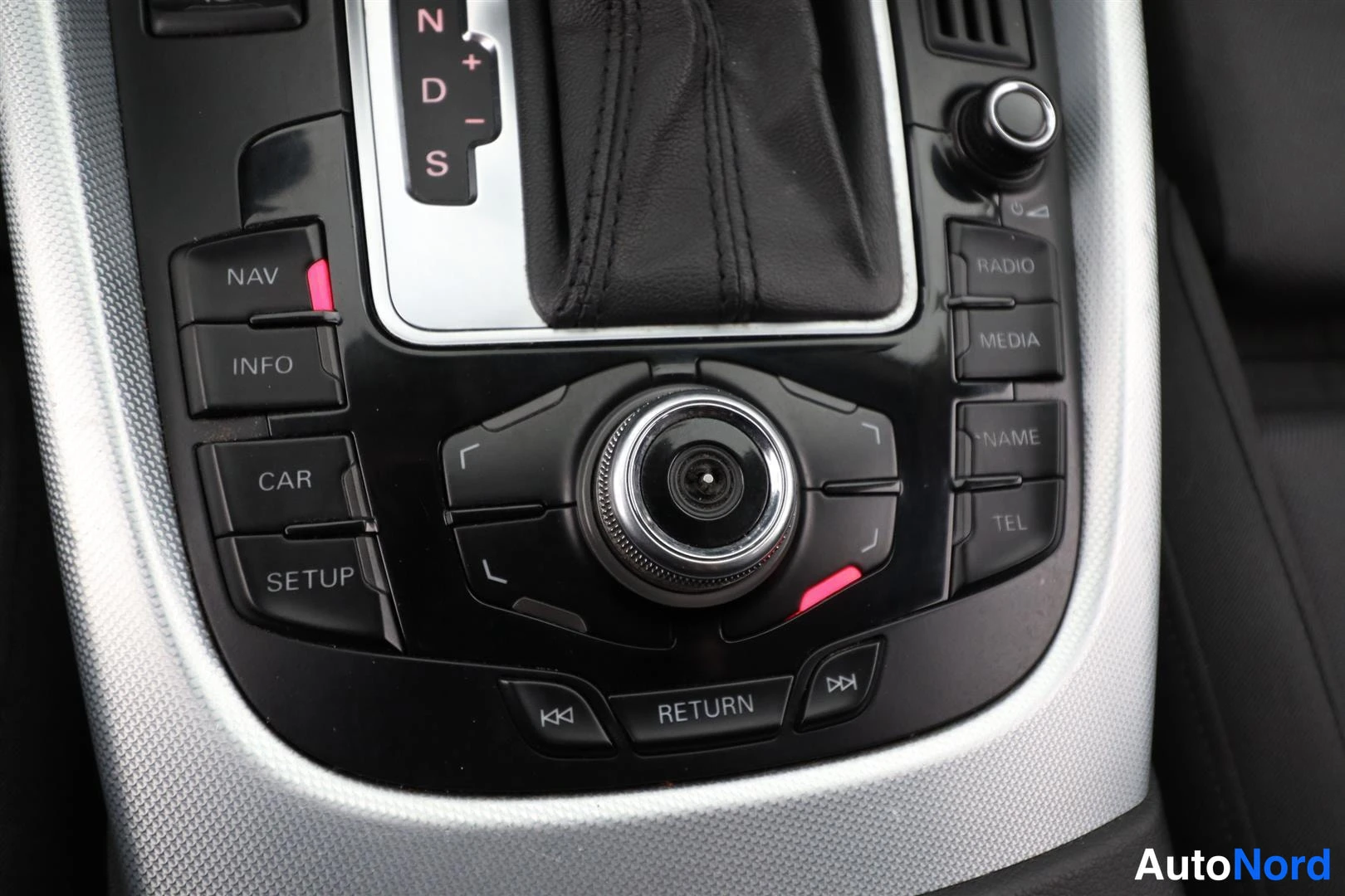 Yksityiskohta: Keskikonsolin MMI-ohjain nuppeineen ja painikkeineen: NAV, INFO, CAR, SETUP, RADIO, MEDIA, NAME, TEL, RETURN.