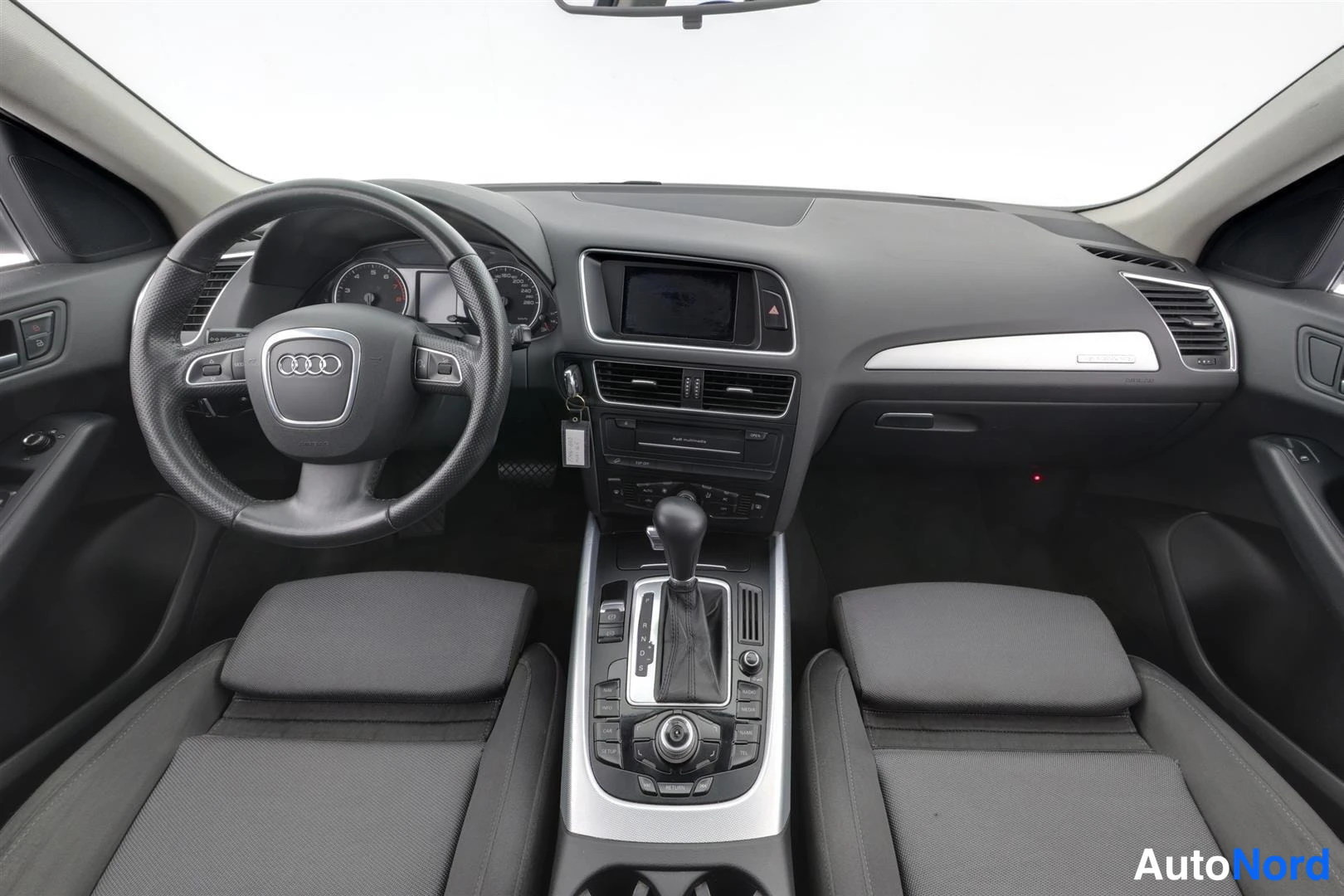Muu: Kojetaulun näkymä ovista: Audi-ohjauspyörä, mittaristo, keskinäytöllä varustettu kojetaulu ja automaattivaihteen valitsin keskikonsolissa, tummat kankaiset etui