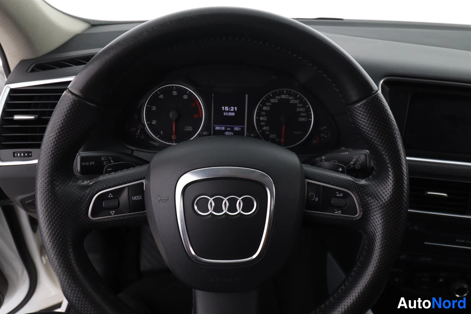 Yksityiskohta: Ohjauspyörä Audi-merkillä ja instrumenttien kierrosmittari, nopeusmittari sekä tumma näyttö.