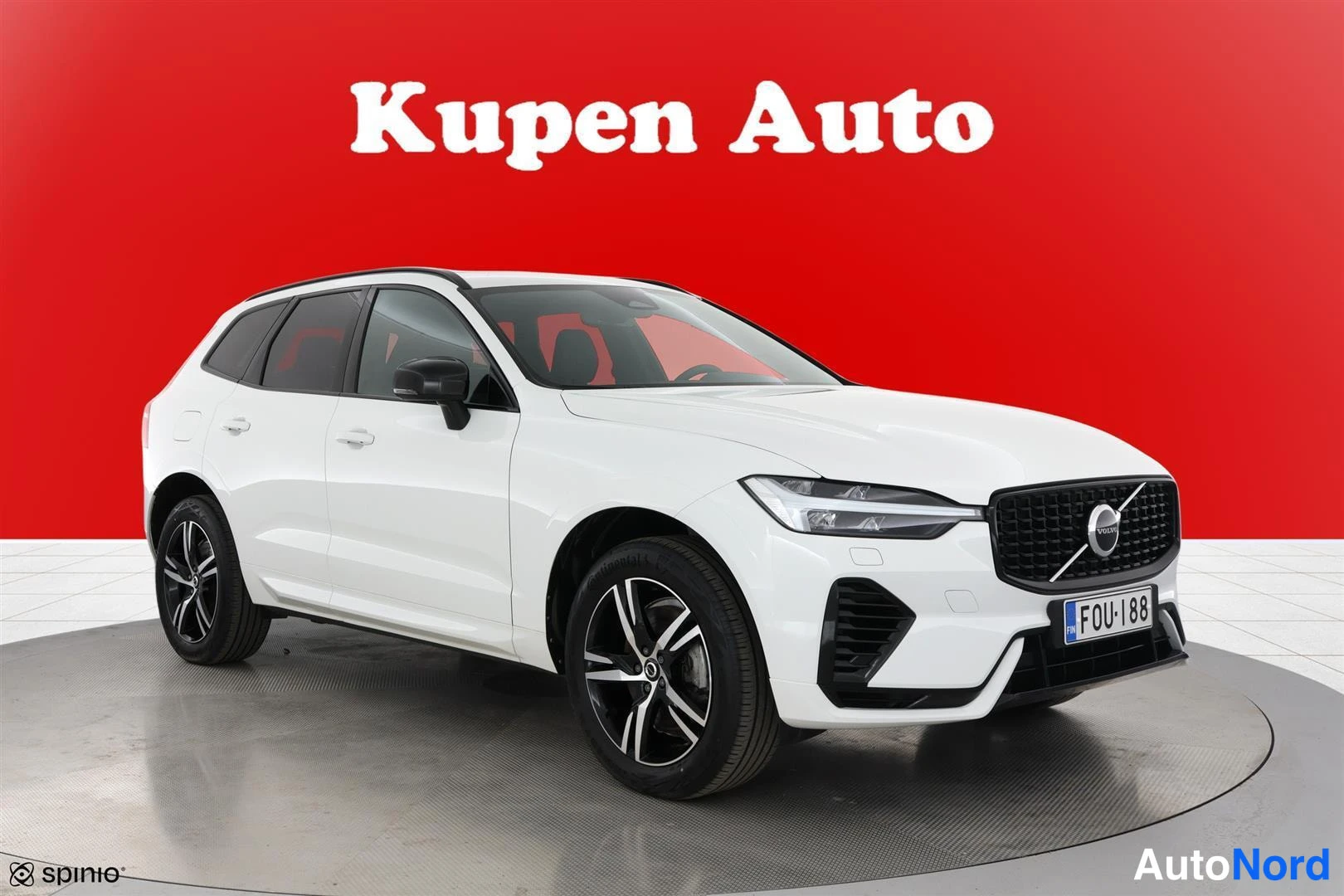 Etuviisto, nokka oikealle: Valkoinen Volvo XC60 farmari etuviistosta punaisella taustalla Kupen Auton tiloissa.