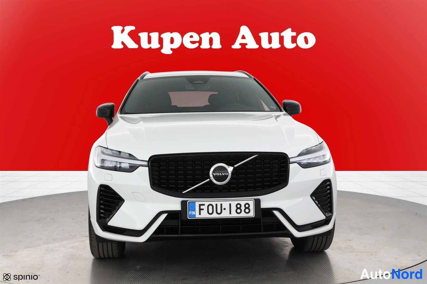 Edestä: Valkoisen Volvo XC60:n etunäkymä, musta etusäleikkö ja Volvo-merkki punaisella taustalla.
