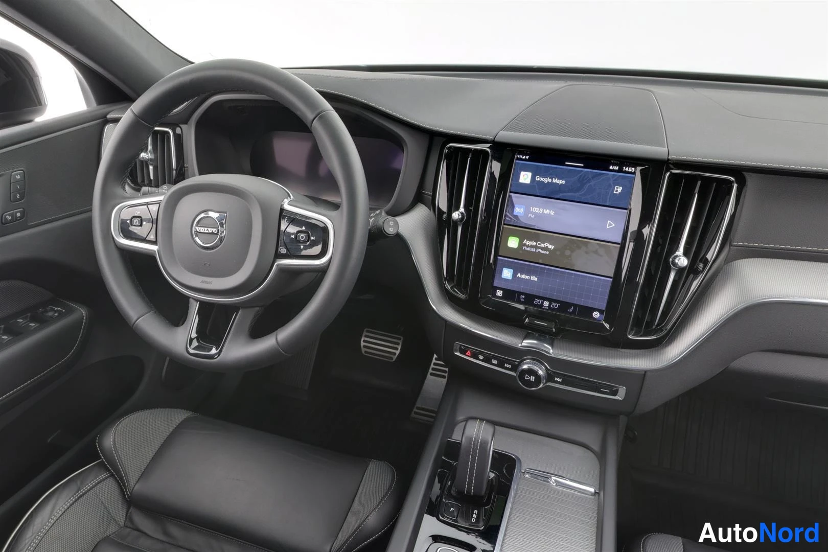 Ohjaamo: Volvo-ohjauspyörä, keskellä kosketusnäyttö, jossa Apple CarPlay ja navigaatio näkyvissä, mustat penkit