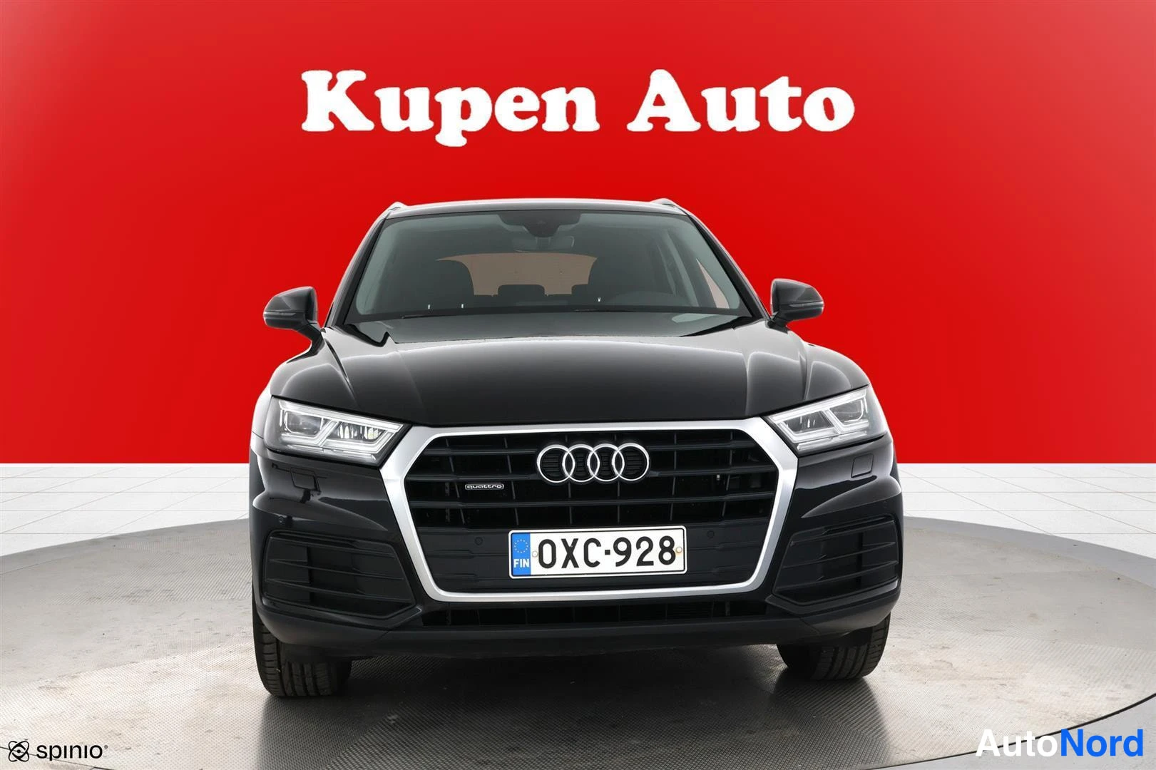 Edestä: Musta Audi Q5 suoraan edestä, rekisteri, punainen tausta.