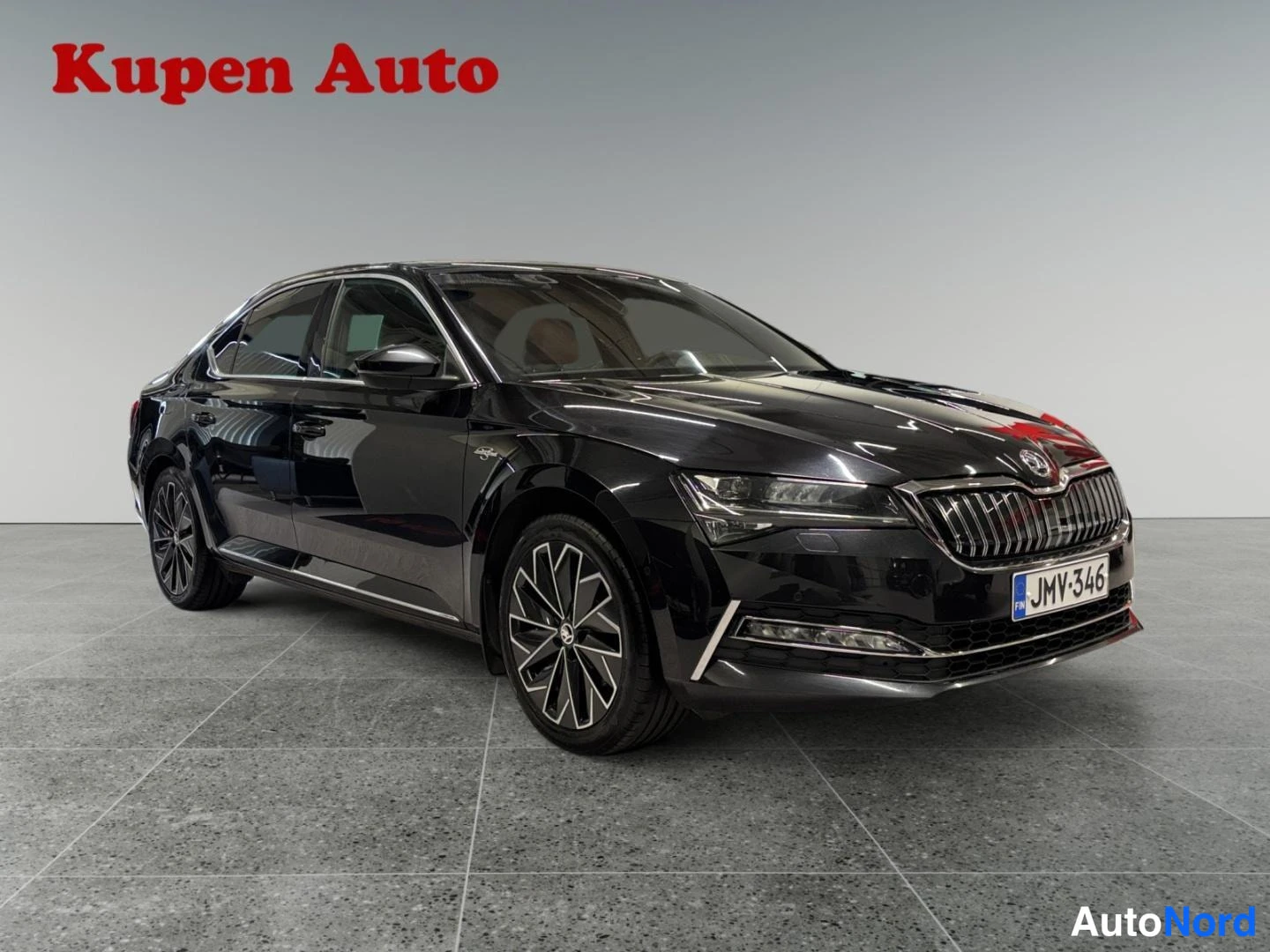 Etuviisto, nokka oikealle: Musta Skoda Superb -sedan edestä ja oikea kylki näkyvissä, etusäleikkö ja kilpi studiotauustassa.