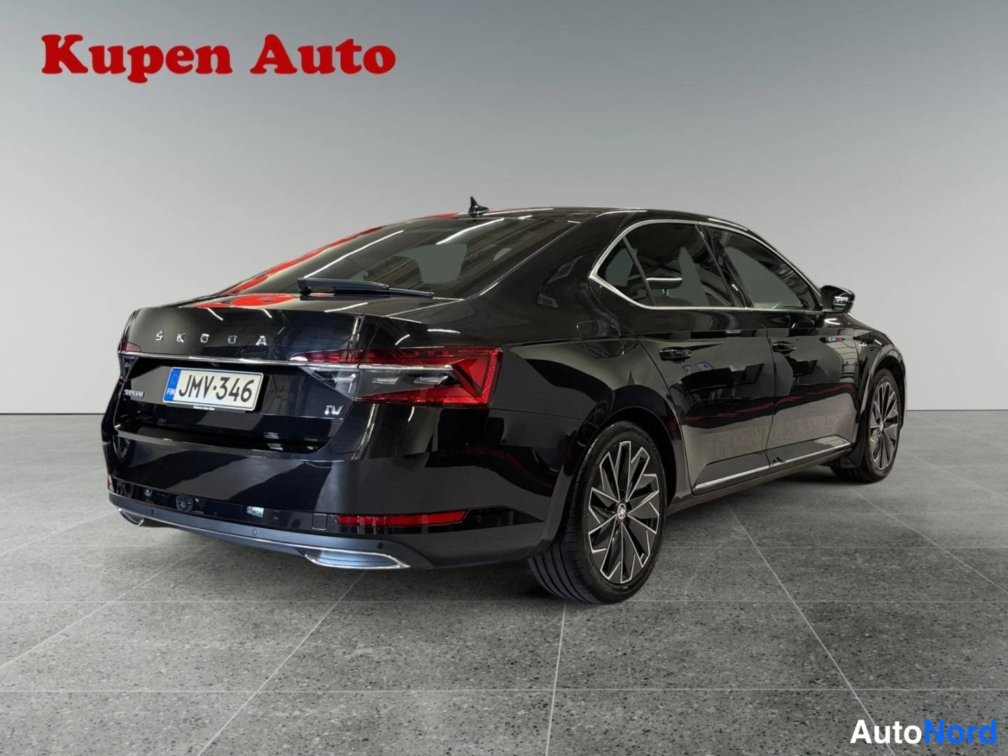 Takaviisto: Mustan Skoda Superb -sedanin takaosa ja oikea kylki, takavalo ja kilpi näkyvissä studiohallissa.