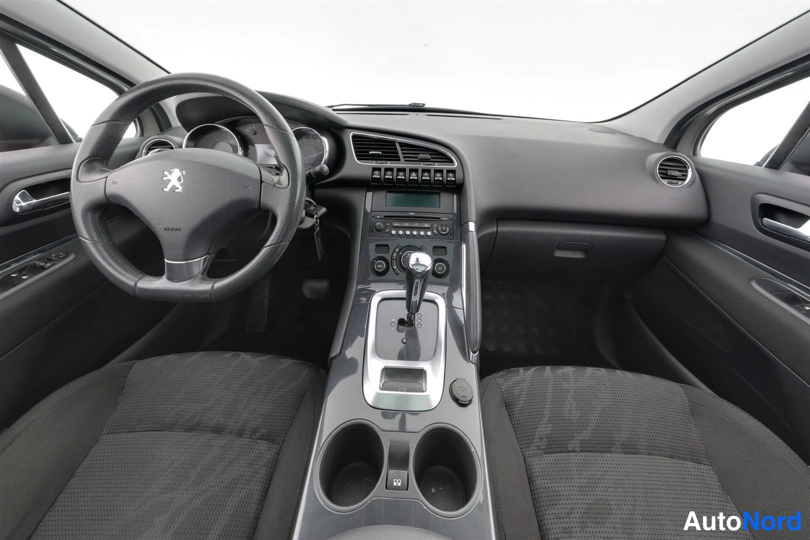 Muu: Auton sisätilat eteenpäin: Peugeot-ohjauspyörä, tumma kojelauta, radiopaneeli ja automaattivaihteen valitsin keskikäyttöineen.