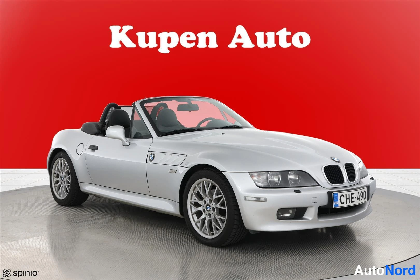 Etuviisto, nokka oikealle: Hopeanvärinen BMW Z3 Roadster avokatto alaspainettuna, kuvattu edestä vasemmalta kolmivARTeelokulmassa punaisella taustalla.