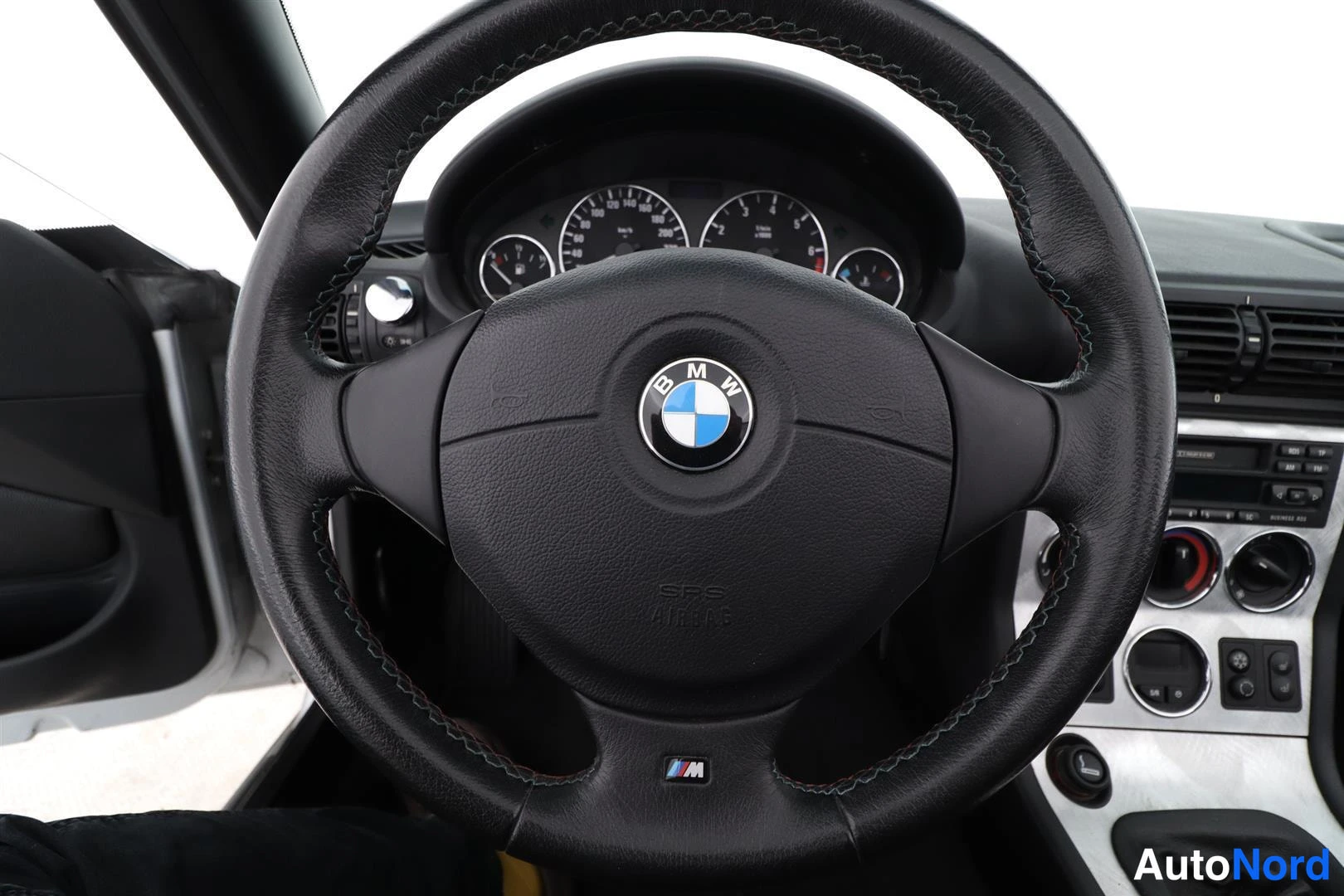 Ohjaamo: Ohjauspyörä BMW-logolla ja M-merkillä, takana mittaristo ja keskikonsoli.