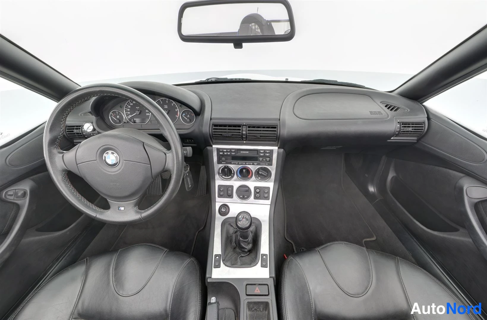 Ohjaamo: Ohjaamo kuvattuna keskeltä: BMW-ohjauspyörä, kojelauta, manuaalivaihto ja kaksi mustaa istuinta
