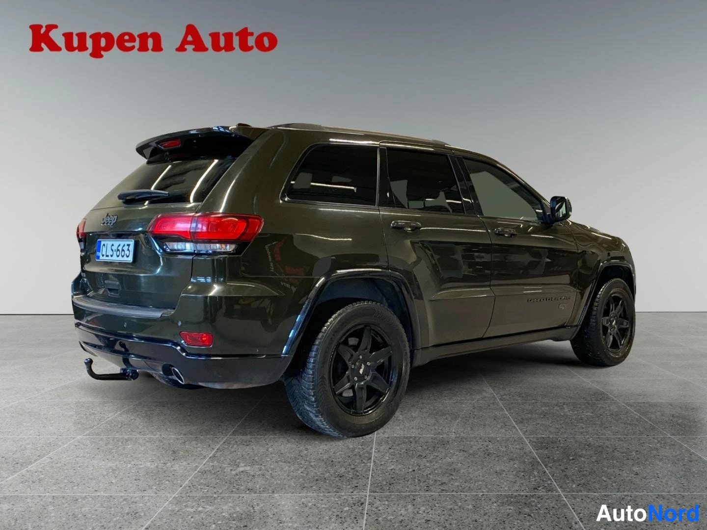 Takaviisto: Tummanvihreä Jeep Grand Cherokee takaa oikealta kuvattuna, rekisterikilpi ja mustat vanteet.