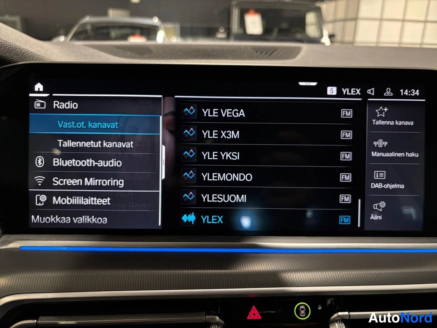 Yksityiskohta: Auton keskikonsolin infotainment-näyttö, jossa radion kanavaluettelo (YLE VEGA, YLE X3M, YLE YKSI, YLEMONDO, YLESUOMI, YLEX) ja valikot kuten Bluetooth-audio ja