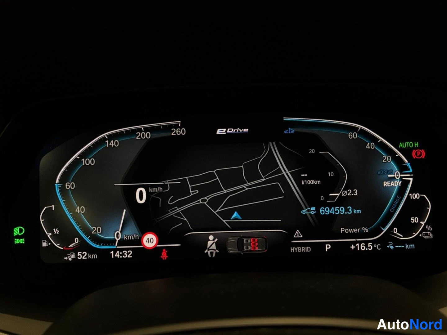 Yksityiskohta: BMW:n digitaalinen kojelauta pimeässä: nopeus 0 km/h, matkamittari 69459,3 km, vaihde P, HYBRID-tila ja ulkolämpötila +16,5 °C.