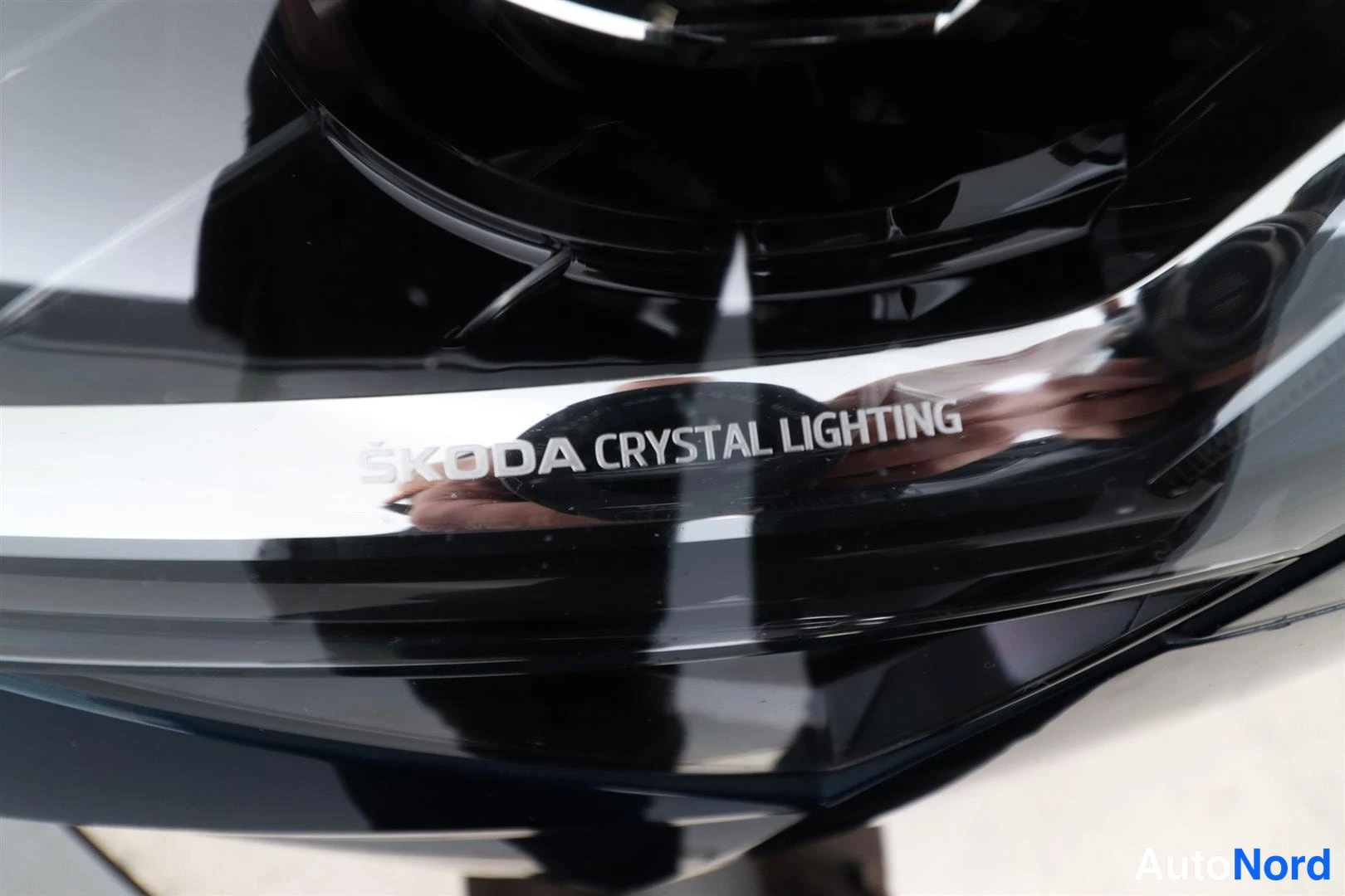 Muu: Ajovalaisimen lähikuva, jossa kiiltävällä pinnalla lukee ”ŠKODA CRYSTAL LIGHTING”.