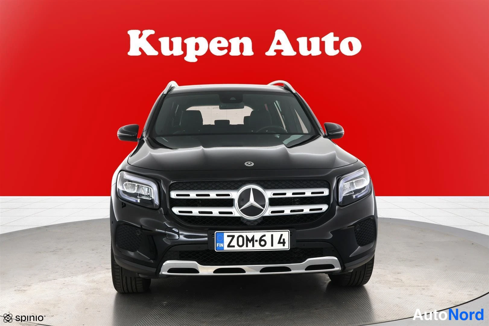 Edestä: Mustan Mercedes-Benzin etunäkymä punaisella taustalla.