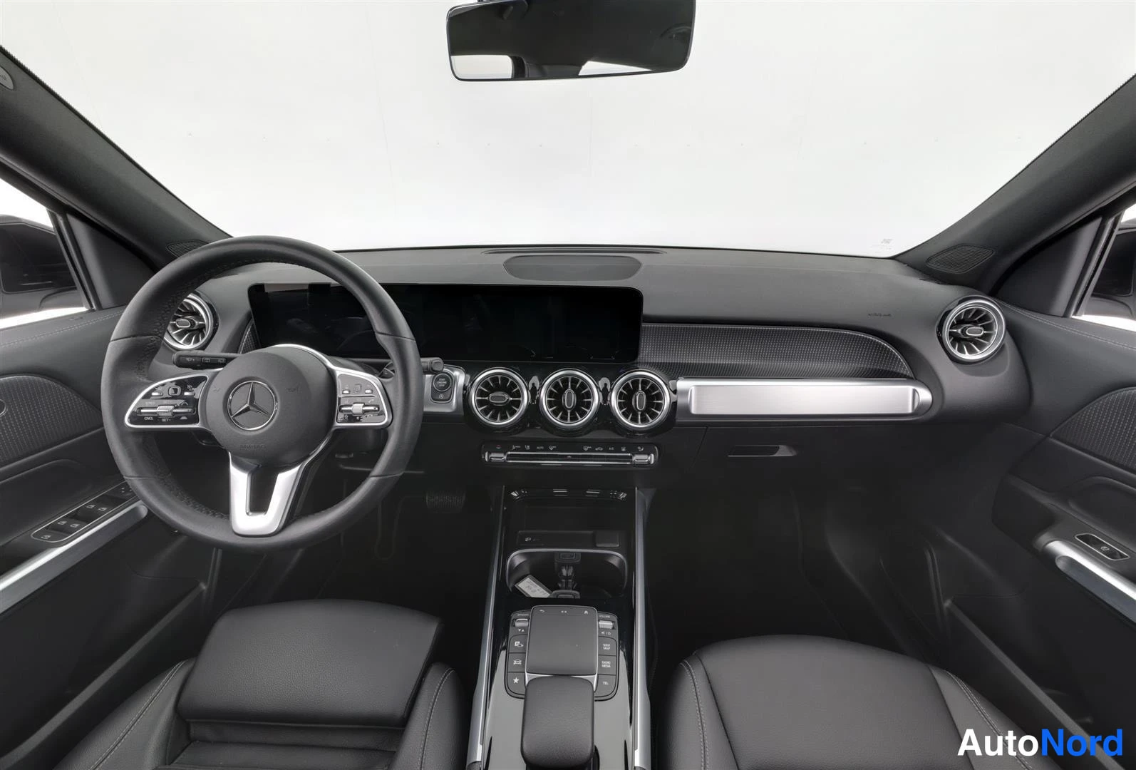 Muu: Mustan auton ohjaamo edestä: Mercedes-ohjauspyörä, keskikäyttönäyttö, pyöreät ilmastointisuuttimet.