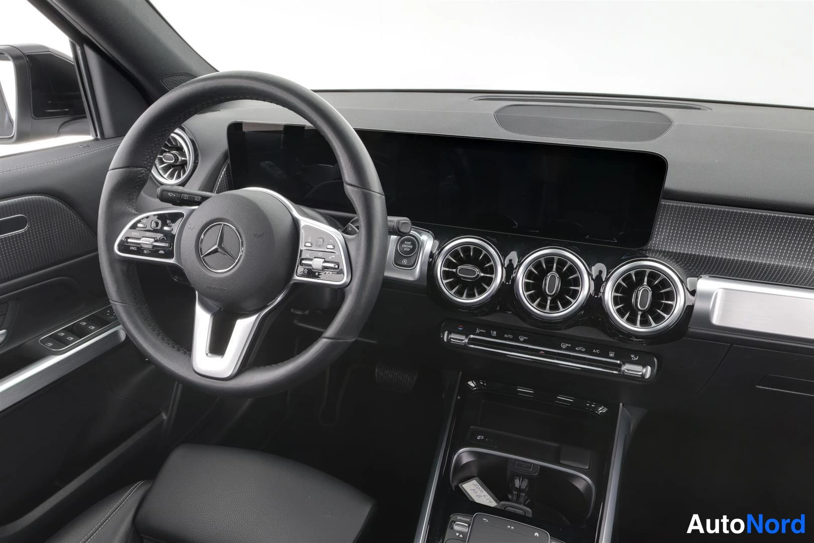 Muu: Ohjaamo lähi Kuva vasemmalta: Mercedes-ohjauspyörä, tumma infotainment-näyttö, kolme pyöreää suutinta.