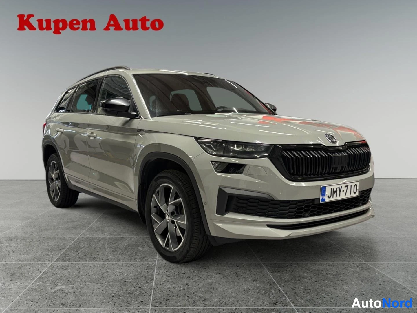 Etuviisto, nokka oikealle: Vaaleanharmaa Skoda Kodiaq edestä kolmivartalonäkymästä, musta etusäleikkö ja rekisterikilpi näkyvät.