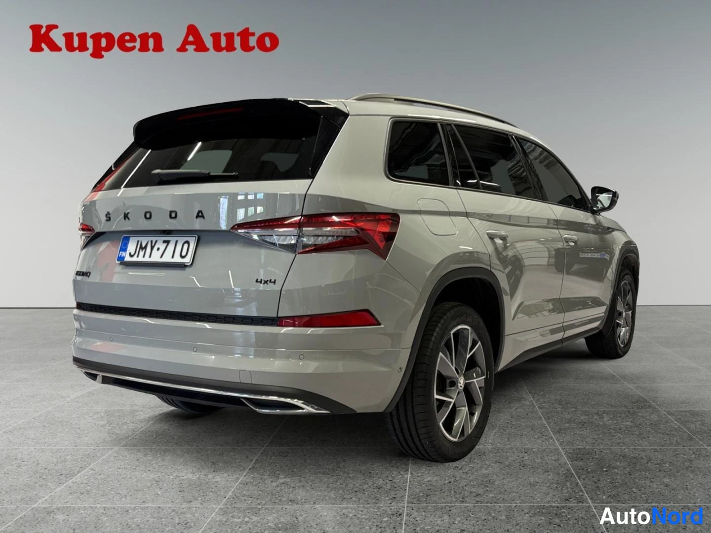 Takaviisto: Vaaleanharmaa Skoda Kodiaq takaa kolmivartalonäkymästä, takavalot, 4x4-merkintä ja rekisterikilpi näkyvät.