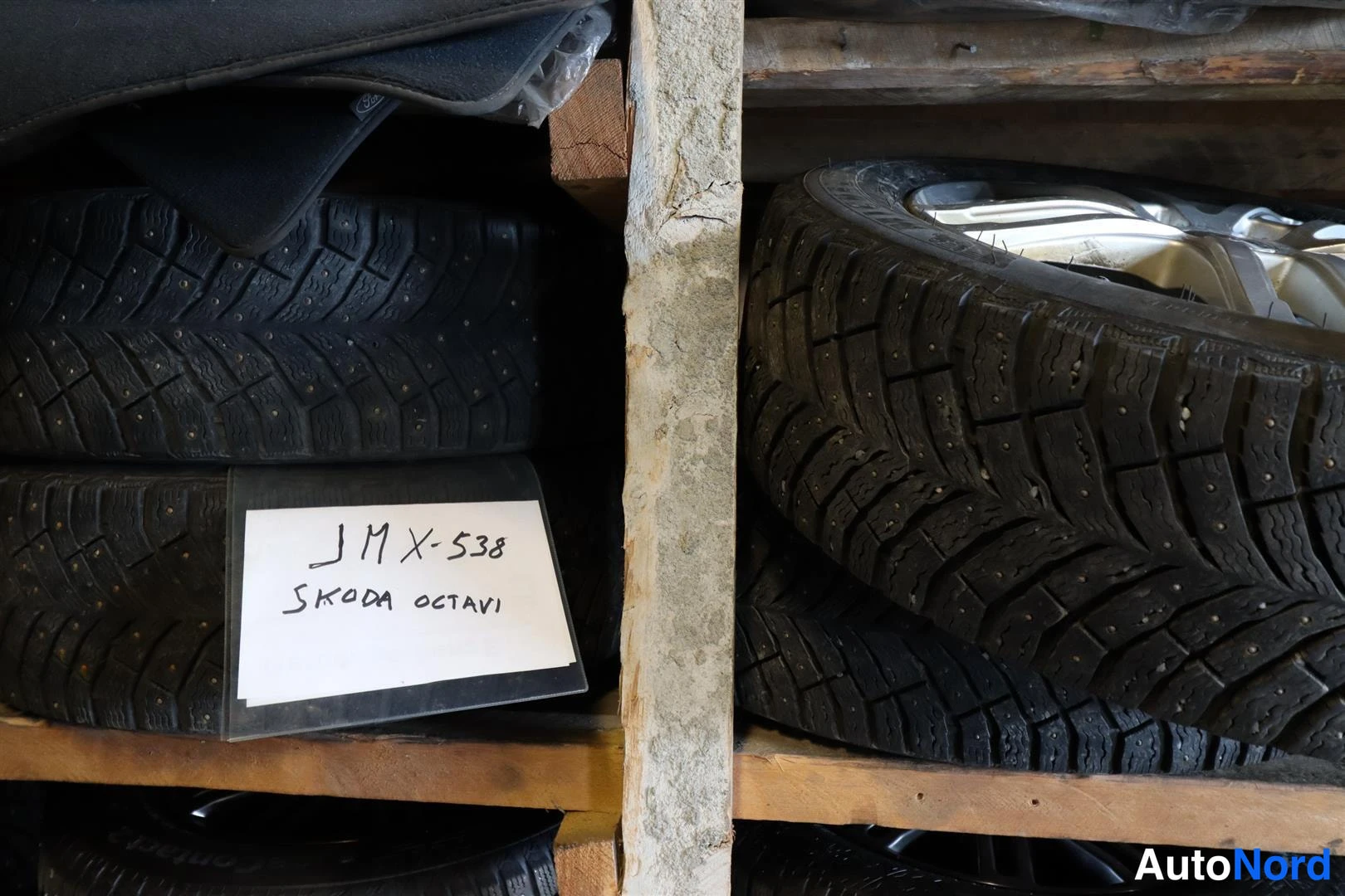 Yksityiskohta: Varastohyllyllä kaksi pinoon asetettua nastarenkassarjaa ja käsin kirjoitettu lapullinen tekstillä SKODA OCTAVI.