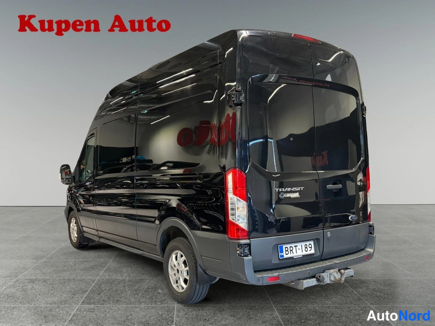 Takaviisto: Mustan Ford Transit -pakettiauton takaosa ja oikea kylki, takaluukussa TRANSIT-teksti ja rekisteritunnus, takana vetokoukku.