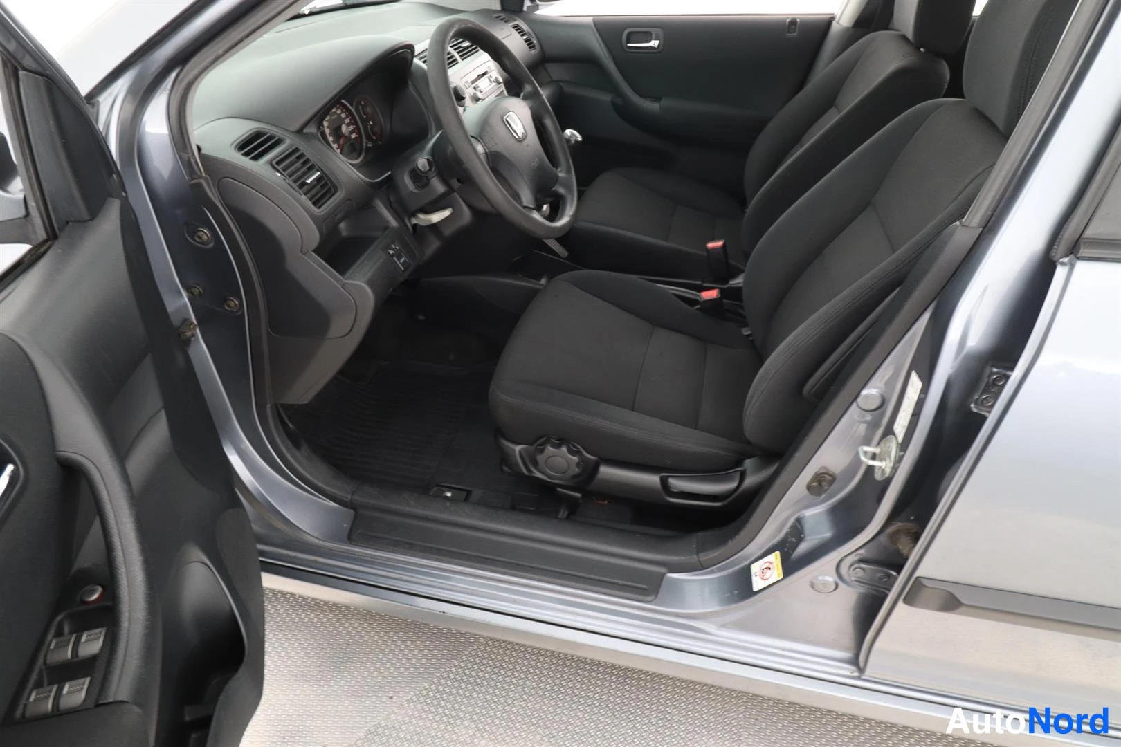Muu: Avatun etioven kautta kuvattu kuljettajan puolen etuistuin, ratin ja kojelaudan näkymä; Honda-merkki ratissa.