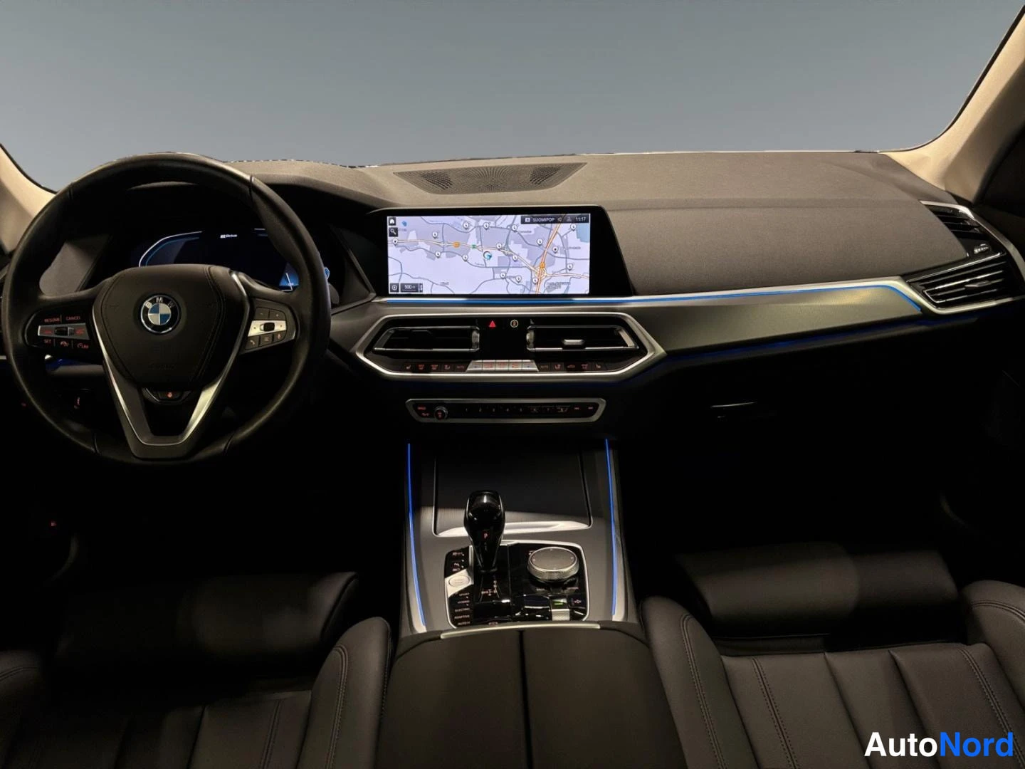 Muu: BMW:n kuljettajan näkymä kojelautaan ja keskikonsoliin: ohjauspyörä, kartta infotainment-näytöllä ja automaattivaihteen valitsin.