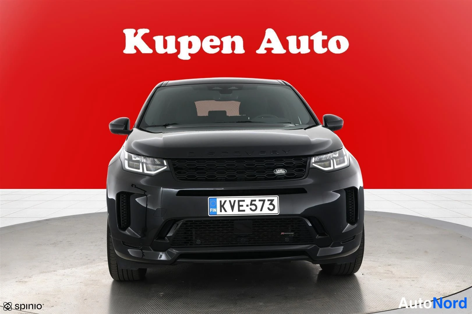 Edestä: Land Rover Discovery Sport musta suoraan edestä; etusäleikkö, ajovalot ja rekisteritunnus näkyvissä.