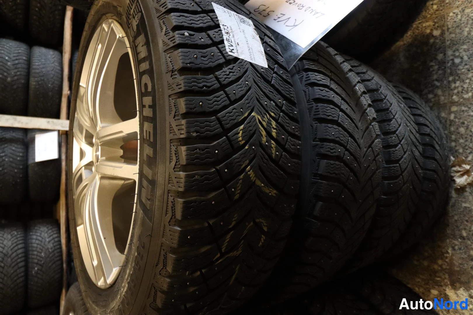 Yksityiskohta: Pinossa Michelin-nastarenkaat alumiinivanteilla; renkaaseen kiinnitetty lappu, jossa lukee.