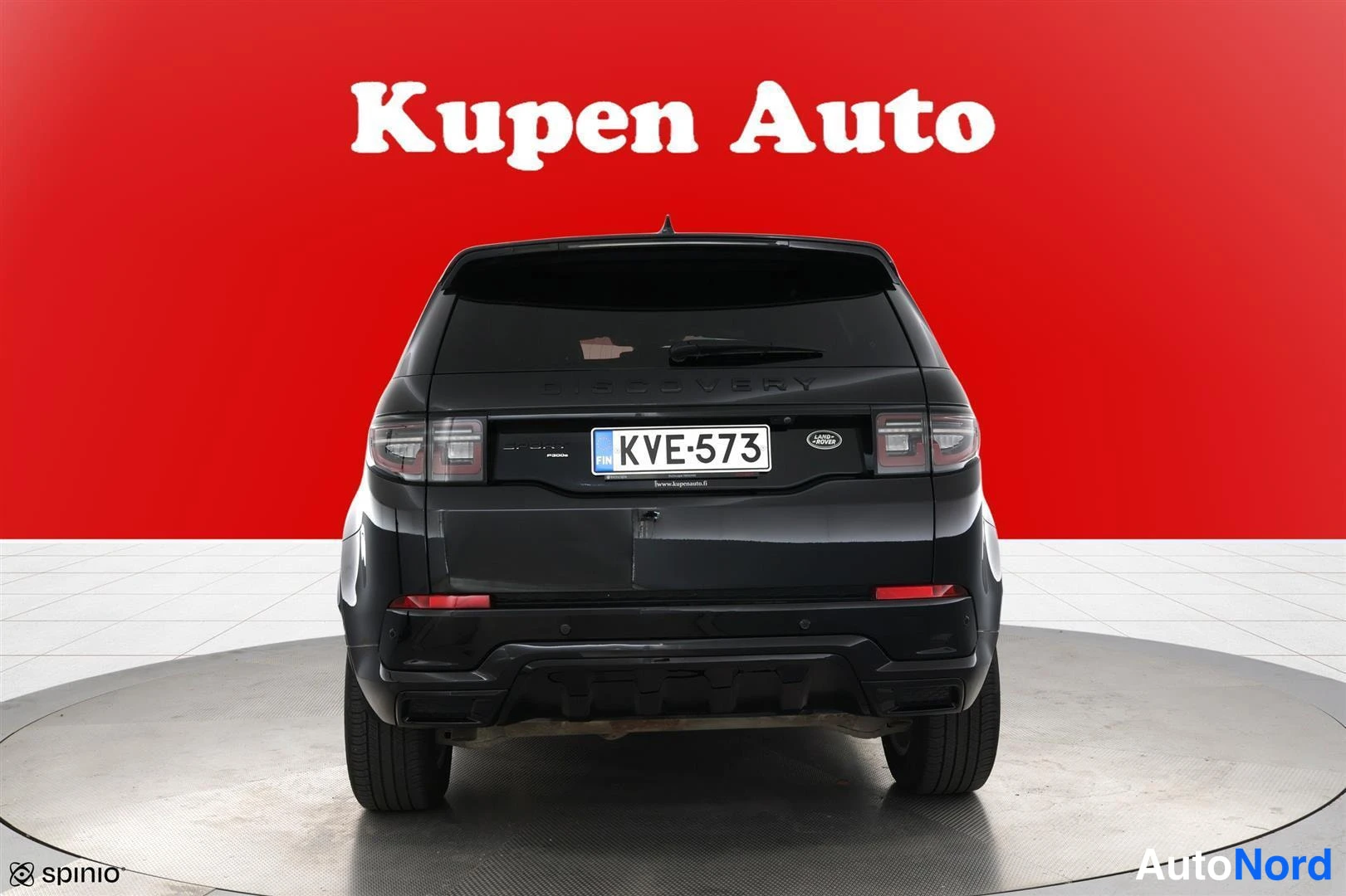 Takaa: Mustan Land Rover Discovery Sportin takaa päin otettu kuva, rekisterikilpi, punainen tausta.