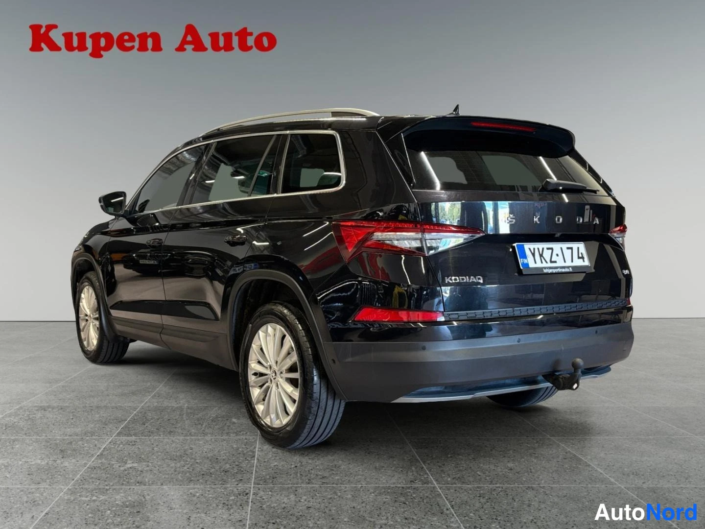 Takaviisto: Mustan Skoda Kodiaq -auton takakulma sisätiloissa; takana näkyy SKODA- ja KODIAQ-tekstit, rekisteritunnus ja vetokoukku.