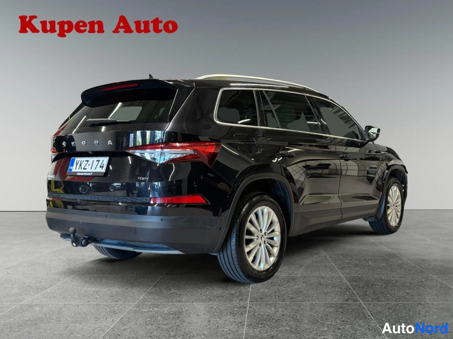 Takaviisto: Mustan Skoda Kodiaq -auton takakulma vasemmalta sisätiloissa; takaluukussa SKODA-teksti, rekisteritunnus ja vetokoukku.