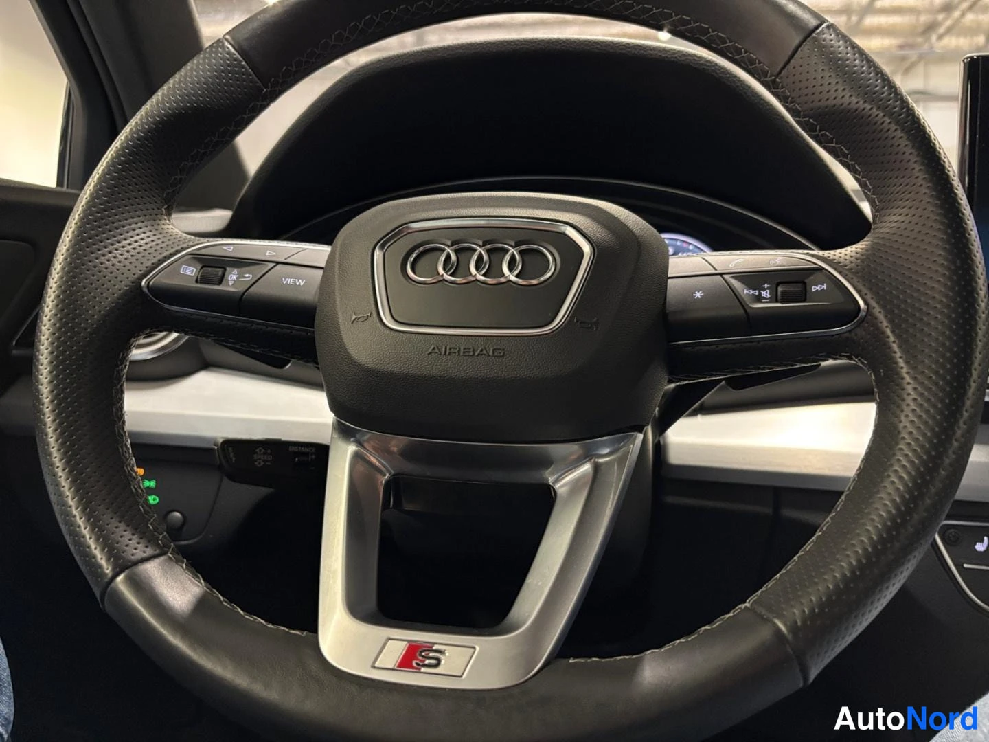 Yksityiskohta: Ohjauspyörä ja S-merkki, vasemmassa puhkimessa AUDI-logo.