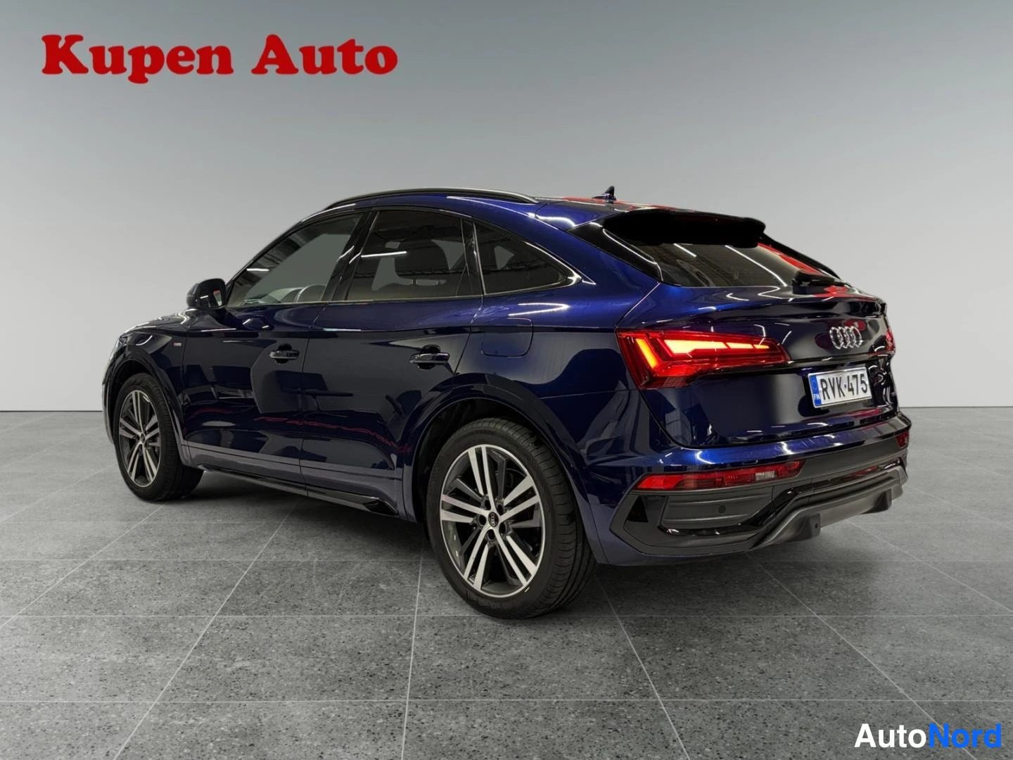 Takaviisto: Sininen Audi Q5 Sportback kulmittain takaa vasemmalta kuvattuna myyntihallissa.